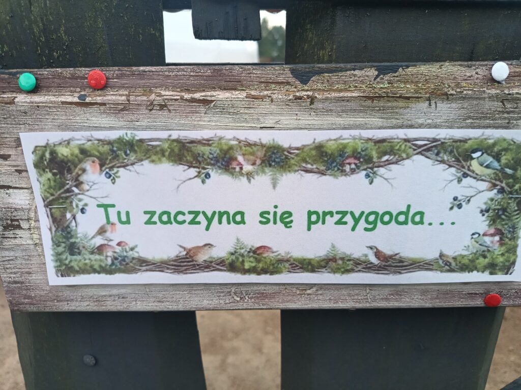 Leśna tablica z napisem „Tu zaczyna się przygoda”